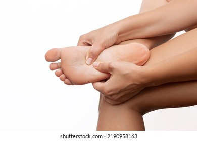 Pain In The Feet. A Woman Holds A Sore Foot With Hand Pressing With Her Hands Isolated On A White Background. Ache Caused By Wearing Uncomfortable Shoes. Orthodontics. Cramp, Spasm