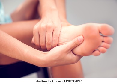 Pain In The Foot, Girl Holds Her Hands To Her Feet, Foot Massage, Cramp, Muscular Spasm, Red Accent On The Foot, Close-up