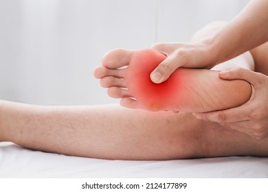 Pain In The Foot, Man Holds Hands To His Feet, Foot Massage, Cramp, Muscular Spasm, Red Accent On The Foot, Close-up
