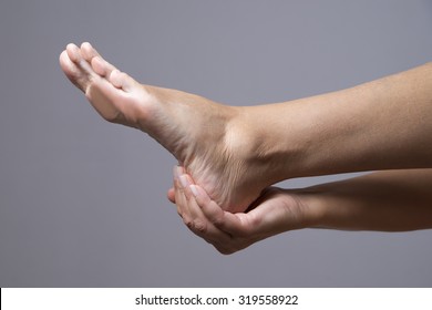 Pain in the foot. Massage of female feet on a gray background
