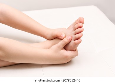 Pain in the foot and toes from uncomfortable shoes. A small kid holds a sore foot with his hands on a white background. Pathology of bone structures, flat feet. Injury, cramp, spasm. Orthodontics