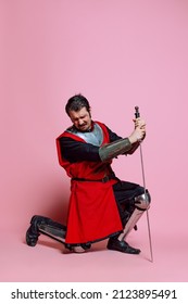 Pain, Sadness. One Young Man, Medieval Warrior Or Knight Wearing Wearing Armor Clothing Posing Isolated Over Pink Background. Model With Wounded Face. Comparison Of Eras, History, Funny Meme Emotions