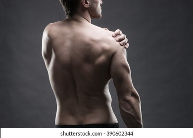 Pain in the shoulder. Muscular male body. Handsome bodybuilder posing on gray background. Low key close up studio shot