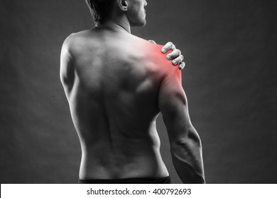 Pain in the shoulder. Muscular male body. Handsome bodybuilder posing on gray background. Black and white photo with red dot