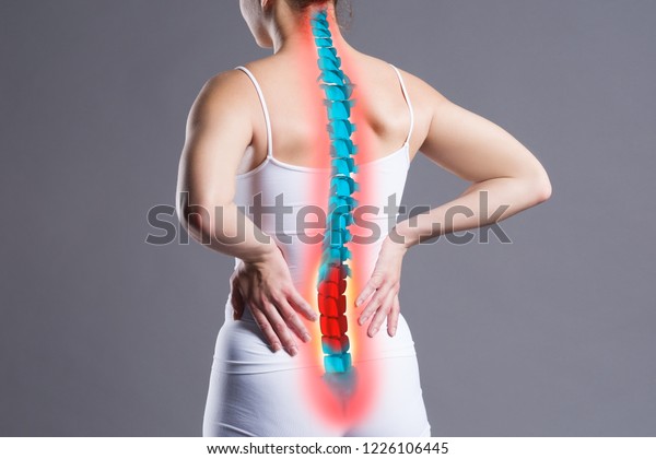 Pain in the spine, woman\
with backache on gray background, back injury, photo with\
highlighted skeleton