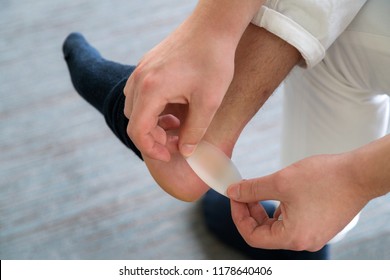 Painful Heel Wound On Mans Feet Caused By New Shoes. Mans Hands Applying Plaster On Terrible Blister On Human Heel. Wet Bloody Painful Skin On Man Foot With Medical Plaster