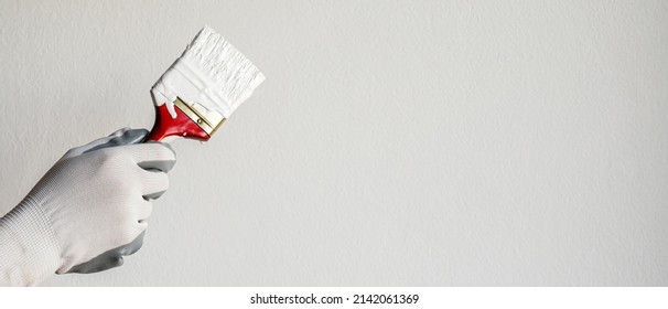 Paint brush, close up hand painter worker painting on surface wall Painting apartment, renovating with white color paint. Leave empty copy space to write descriptive text beside.