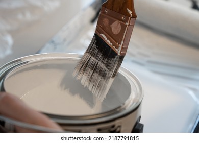 Paint Brush Is Scraped On Edge Of Paint Can To Remove Excess White Paint