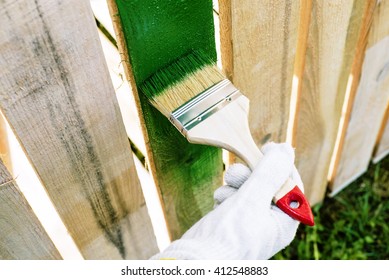 Paint Brush With Wooden Handle And Dab Of Green Paint , Painting Wooden Furniture, Close Up, Hand In Protective Glove Cotton Brush Paints The Wooden Fence, A Painter Paints Construction