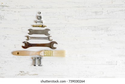 Paint brush wrench, nuts and bolts decorated as Christmas tree on a white wooden background. Christmas greeting card and Happy new year greeting card concept. Top view with copy space for your text