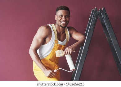 With Paint Brush. Young African American Worker In The Yellow Uniform 