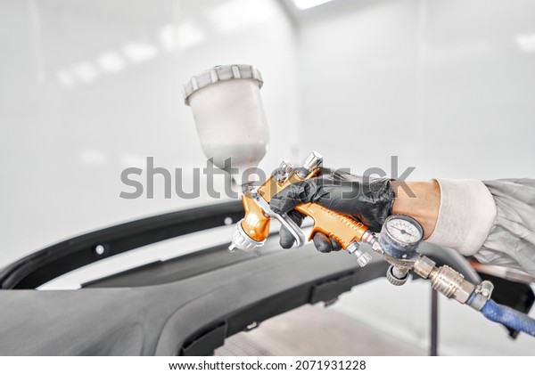 Paint Gun is designed by professionals for a\
professional quality paint job. Worker painting parts of the car in\
special painting chamber, wearing costume and protective gear. Car\
service station.