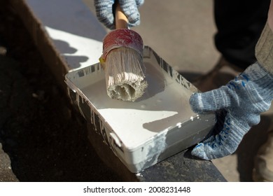 Paint On The Brush. Round Brush With White Paint. Painting The Curbs Along The Road. Marking On The Kerb Stone.