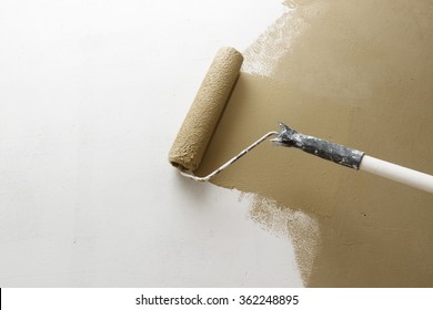 Paint roller applying brown paint on white wall, home improvements, horizontal view with copy space
