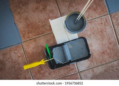 Paint Roller With Brush And Tray Next To Open Pot Of Paint Shot From Above Surrounded By Terracotta Floor Tiles Being Painted Gray, Diy And Home Renovation Concept