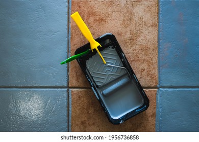 Paint Roller With Brush And Tray Next To Open Pot Of Paint Shot From Above Surrounded By Terracotta Floor Tiles Being Painted Gray, Diy And Home Renovation Concept