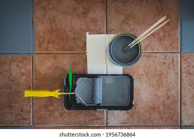 Paint Roller With Brush And Tray Next To Open Pot Of Paint Shot From Above Surrounded By Terracotta Floor Tiles Being Painted Gray, Diy And Home Renovation Concept