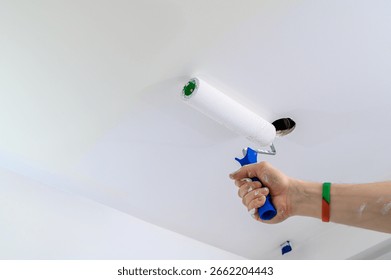 A paint roller dabbed with white paint while painting a wall, close-up