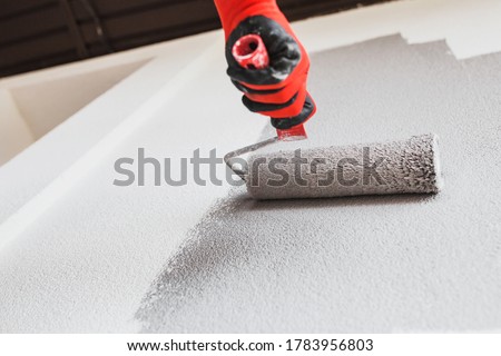 Paint roller on the wall during painting - renovation of the building facade in dark gray