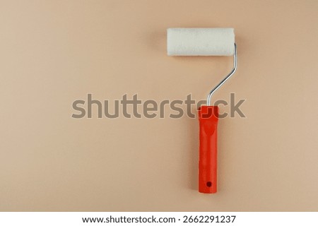 Paint roller with red handle on beige background for home decoration and DIY painting concept