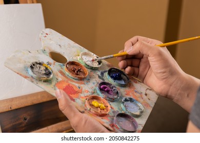 paint stained hand holding a brush, artist mixing colors on a palette, work tools, hobbie, creative lifestyle in studio, colorful water paint texture - Powered by Shutterstock