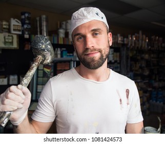 Paint Store Employee Holding Paint Covered Hammer And Smirking