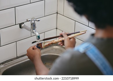 Paint, water and artist cleaning paintbrush under a tap or faucet. Clean, painter and creative woman washing her brushes with hands in the sink in her studio. Clean up after painting artwork project - Powered by Shutterstock
