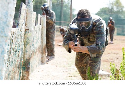 Paintball Player In Camouflage And Mask Aiming With Gun In Shootout Outdoors

