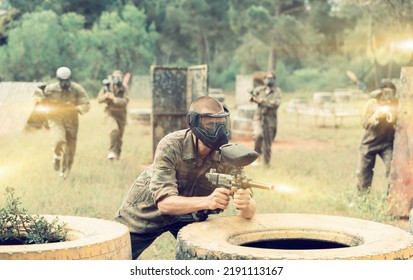 Paintball Player In Camouflage And Mask Aiming With Gun In Shootout Outdoors