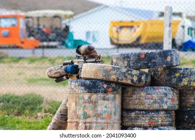 Paintball player positioned against rubber barriers. Paintball player in blue gloves and uniform. Ready to fire. Garden hobby sport.