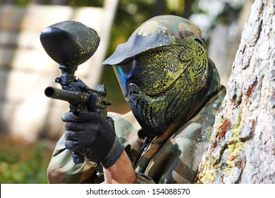 paintball player in protective uniform and mask aiming gun before shooting in summer