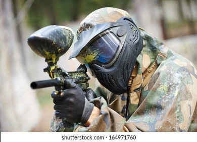 paintball player in protective uniform and mask aiming gun before shooting in summer