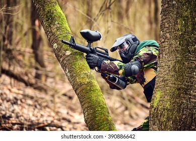 Paintball player in protective uniform and mask aiming gun in the forrest cover