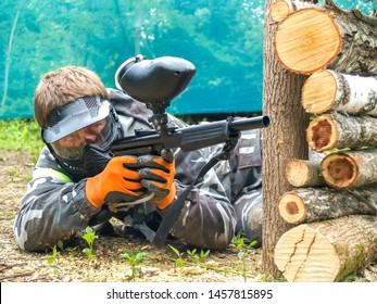 A paintball player who is ready to shoot from hiding. Lying on the ground and shooting. Immediately before shooting with a gun. Paintball player in protective uniform and mask