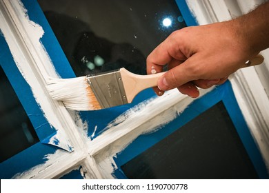 Paintbrush Hand Painting White Paint Or Primer On To Tape Prepped Window Frame.