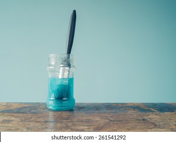 A paintbrush is soaking in a jar of blue water - Powered by Shutterstock