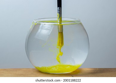 A paintbrush with yellow paint is dipped in a jar of water on a white background. The paint spreads in the water. - Powered by Shutterstock