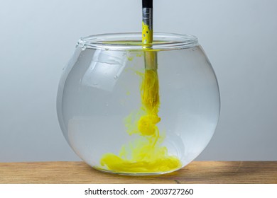 A paintbrush with yellow paint is dipped in a jar of water on a white background. The paint spreads in the water. - Powered by Shutterstock