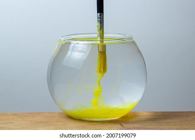 A paintbrush with yellow paint is dipped in a jar of water on a white background. The paint spreads in the water. - Powered by Shutterstock