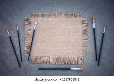 Paintbrushes and blank canvas with copy space on gray concrete background.