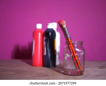 Paintbrushes in a glass jar on pink background wide selective focus  - Powered by Shutterstock