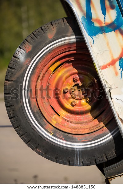 Painted\
car wheel. Detail of the old automobile. Car is set to stand on\
it\'s front, rear wheel is in the air and designed artistically. Gas\
station in Finland, Scandinavia, North\
Europe.