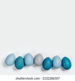 Painted Easter eggs blue, gray colored in row on white background with copy space. Chicken egg natural pastel shades. Easter holiday food top view, minimal design aesthetic flat lay