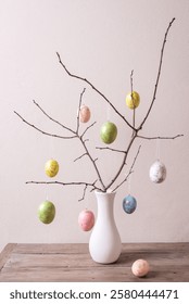 Painted Easter eggs on twigs in white vase, neutral background, minimal composition. Happy Easter decor.