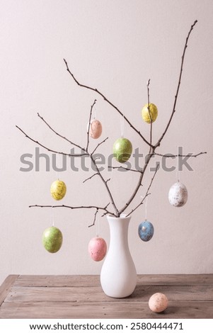 Painted Easter eggs on twigs in white vase, neutral background, minimal composition. Happy Easter decor.