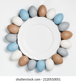 Painted Easter Eggs Pastel Colors Beige, Gray, Blue Around White Empty Plate. Happy Easter Holiday Card, Celebration Food Concept, Chicken Egg Trendy Color. Top View Table, Frame With Copy Space.