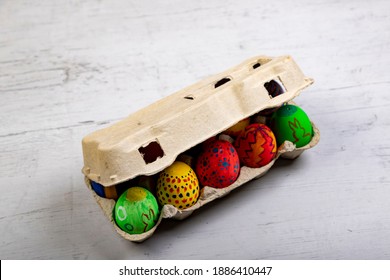 Painted Eggs With Easter Motives In A Closed Egg Carton On A Wooden Board