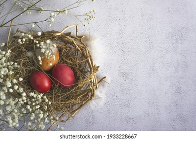 Painted Eggs In A Nest Of Twigs And Dry Grass, A Flowering Branch. Preparing For Easter. From Above. Copy Space...