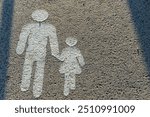 A painted ground image showing a man holding hands with a child, symbolizing a pedestrian walkway. The simple figures, in white, indicate safe crossing for pedestrians.