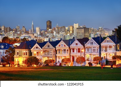 The Painted Ladies of San Francisco, California sit glowing amid the backdrop of a sunset and skyscrapers. - Shutterstock ID 122041915
